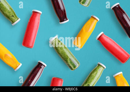 Les smoothies colorés dans des bouteilles en verre sur fond bleu, vue d'en haut. Banque D'Images