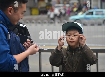 Garçon de neuf ans Ye Jianjun, droite, essaie sur une paire de lunettes d'un journaliste lors d'une pause de sa performance dans une rue de la ville de Changsha, centra Banque D'Images