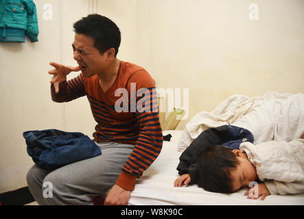 Vous Pinghui, le père de garçon de neuf ans Ye Jianjun, essaie d'ouvrir sa bouche avec un doigt à côté de sa plus jeune fille dormir sur le lit dans un i Banque D'Images