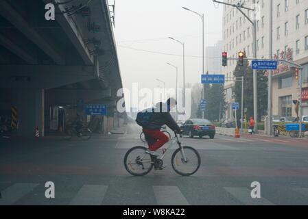 --FILE--un cycliste portant un masque de visage rides sur une route dans le smog lourde à Beijing, Chine, 18 mars 2016. Le smog est éclaircie dans les villes de l'Est de la Chine Banque D'Images