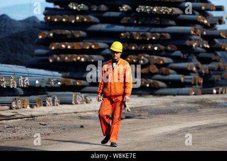 --FILE--Un travailleur chinois passe devant des piles de tiges d'armature en acier sur un quai du port de Qingdao en Qingdao city, province de Shandong en Chine orientale, Banque D'Images