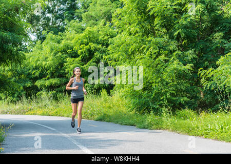 Fille d'exécution runner jogging le sentier du parc de la nature de la formation pendant l'été pour cardio course de marathon ou d'objectif de perte de poids succès. Femme Asiatique de l'athlète avec un corps vivant heureux mode de vie sain. Banque D'Images