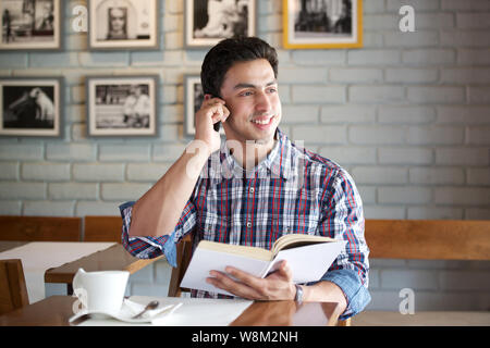 Young man talking on a mobile phone and reading a book in a restaurant Stock Photo