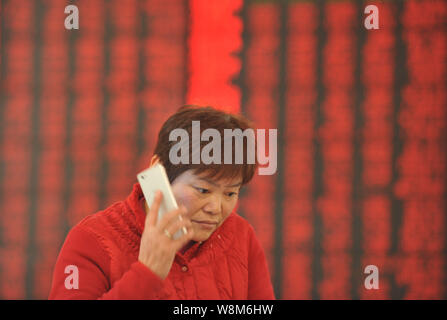 Un investisseur chinois parle sur son téléphone mobile devant un écran pour l'affichage des prix des actions (rouge pour l'augmentation des prix) à une maison de courtage en Fuy Banque D'Images