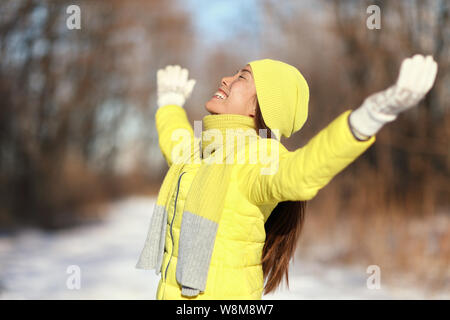 La liberté de la neige heureuse femme insouciante. Femme asiatique relaxante à profiter du soleil sur une journée d'hiver ensoleillée avec des bras jusqu'à l'extérieur, dans la nature des forêts yellow Down veste avec chapeau et écharpe en tricot. Banque D'Images