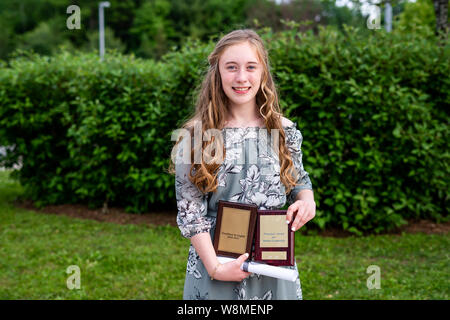 Young teen girl/Middle school student standing in front of a bush/jardin après sa remise des diplômes tout en maintenant un diplôme et prix universitaires. Banque D'Images