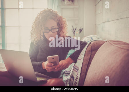 Offres de nos gens au travail à la maison - belle femme de race blanche adultes s'asseoir sur le canapé avec téléphone et ordinateur portable -travail de l'entreprise concept. Banque D'Images