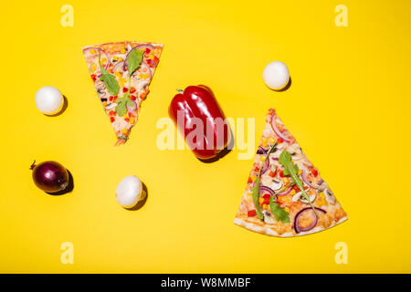 Mise à plat photo de deux tranches de pizza et quelques légumes isolé sur fond jaune Banque D'Images