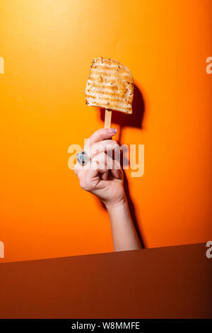 Poulet grillé sur ice cream stick a tenu à la main contre fond orange Banque D'Images