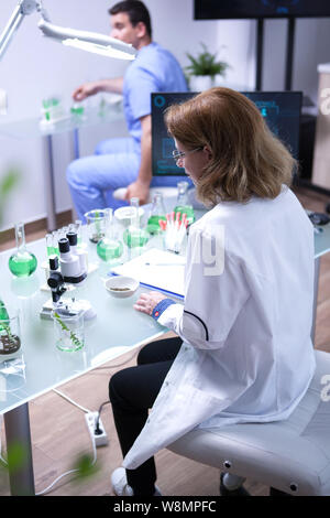 L'âge moyen female scientist en prenant un échantillon de sol pour analyse au microscope pour. Jeune biologiste travaillant dans l'arrière-plan. Banque D'Images