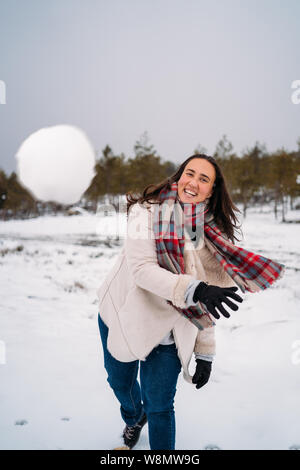 Femme vêtue d'un manteau, smiling, parce qu'elle a jeté une boule de neige à l'appareil photo - Vacances - Vertical image Banque D'Images