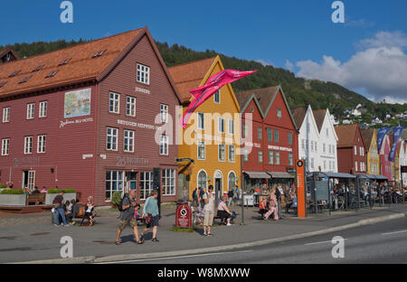 Les touristes s'asseoir au soleil dans les bars et cafés en plein air dans le vieux quai et bâtiments traditionnels en bois dans le quartier de Bryggen, Bergen, Norvège Banque D'Images