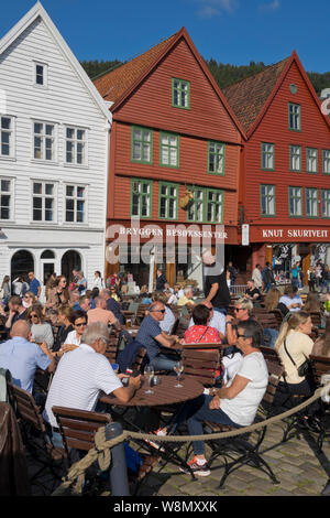 Les touristes s'asseoir au soleil dans les bars et cafés en plein air dans le vieux quai et bâtiments traditionnels en bois dans le quartier de Bryggen, Bergen, Norvège Banque D'Images