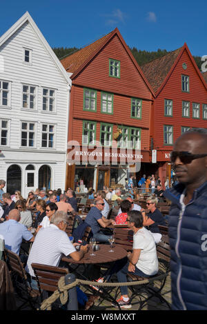 Les touristes s'asseoir au soleil dans les bars et cafés en plein air dans le vieux quai et bâtiments traditionnels en bois dans le quartier de Bryggen, Bergen, Norvège Banque D'Images