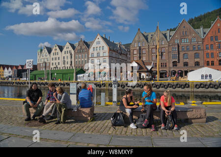 Les touristes s'asseoir au soleil dans les bars et cafés en plein air dans le vieux quai et bâtiments traditionnels en bois dans le quartier de Bryggen, Bergen, Norvège Banque D'Images