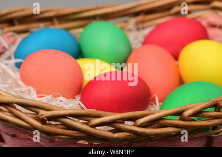 Les oeufs de pâques de diverses couleurs sont dans un panier en osier de près. Photographie horizontale Banque D'Images