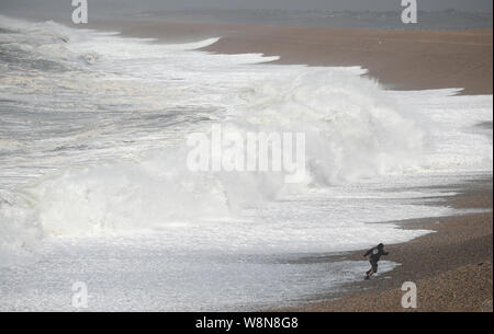 Un homme s'en va former les vagues comme ils s'écrasent contre Chesil Beach dans le Dorset, que le Met Office a mis en place des avertissements d'orages jaune en Écosse et en Irlande du Nord et pour des vents forts à travers le pays de Galles et la plupart de l'Angleterre. Banque D'Images