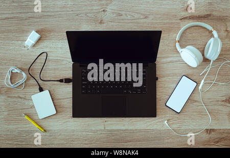 Ordinateur portable avec un disque portable connecté avec des écouteurs et un smartphone sur le bureau. Lieu de détente ou de travail. L'écran du téléphone blanc avec place pour ins Banque D'Images