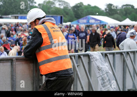 Banbury, Oxfordshire, le 10 août 2019. Gardien de sécurité wearing hard hat pour la sécurité en raison des vents violents et de la mauvaise météo à Fairport Convention's Cropredy festival, Banbury, Oxfordshire, UK Banque D'Images