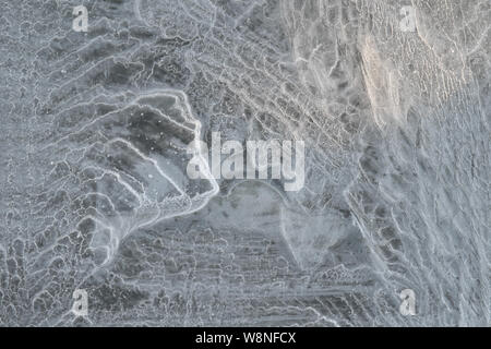 La lumière du soleil met en évidence les lignes de fracture de stress sur la glace dans un étang, révélant une montagne 1 Banque D'Images