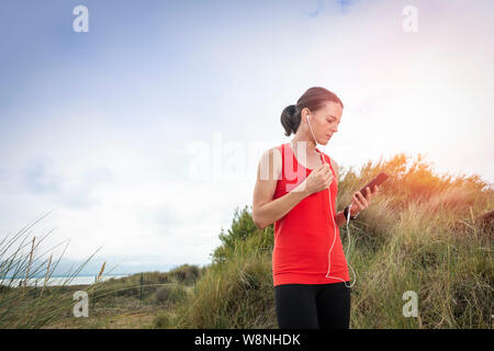 Femme avec casque, écouteurs, contrôler son téléphone portable après l'exercice à l'extérieur Banque D'Images