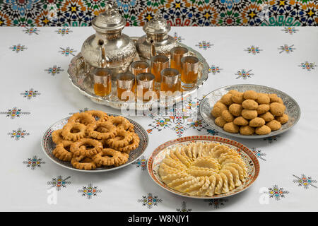 Avec des plats de fête traditionnelle des cornes de gazelle marocaine, des gâteaux et du thé sur une nappe brodée Banque D'Images