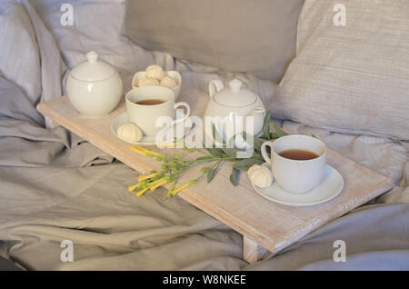 Détendre le petit déjeuner au lit. Théière et deux tasses et les sucreries meringue sur le plateau avec des fleurs. Style scandinave. Banque D'Images