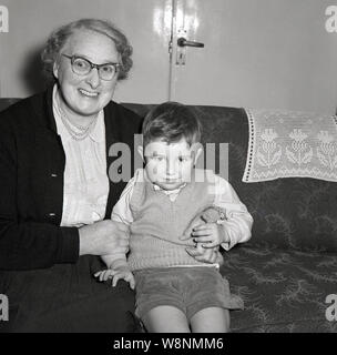 Années 1950, historiques, smartly dressed petit garçon assis à l'intérieur sur un canapé avec sa grand-mère, England, UK. Banque D'Images