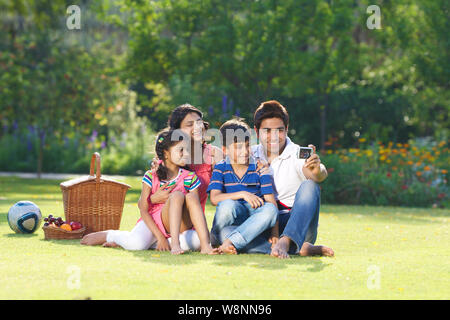 La famille prend une photo d'elle-même avec un appareil photo numérique dans un jardin Banque D'Images