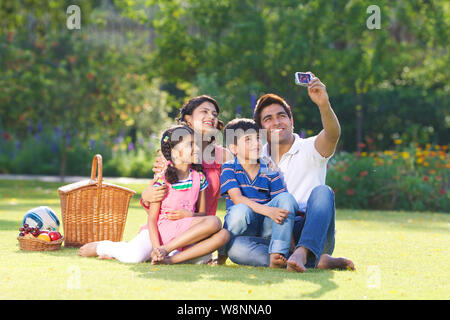 La famille prend une photo d'elle-même avec un appareil photo numérique dans un jardin Banque D'Images