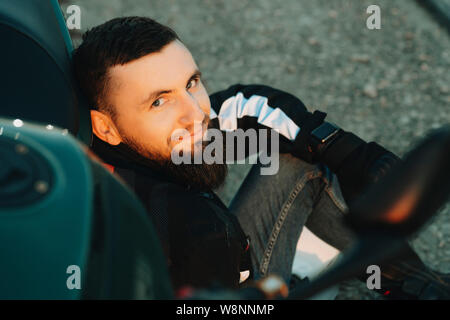 Vue de la récolte de l'heureux jeune homme barbu en Veste motard assis sur la moto à Pise looking at camera Banque D'Images