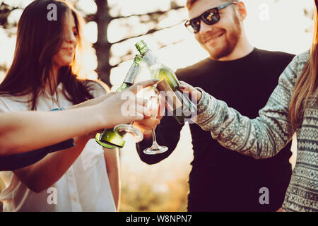 Les jeunes cultures tintement des bouteilles de bière et verres de champagne tout en célébrant le jour ensoleillé dans la nature Banque D'Images