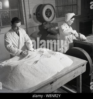 Années 1950, historique, un homme et une femme portant des manteaux blancs qui travaillent à l'entreprise de fournitures médicales d'Arthur H. Cox & Co. qu'ils traitent les matières premières de pilules. Établi à Brighton, Angleterre, en 1839, leur publicité slogan était, 'le comprimé avant tout maison'. Hawker Arthur Cox était un homme d'époque victorienne qui en 1854 un revêtement breveté pearl pour comprimés. En tant que fabricant de produits pharmaceutiques qu'ils ont fournis des chimistes thorougout le Royaume-Uni et le commonwealth. Banque D'Images