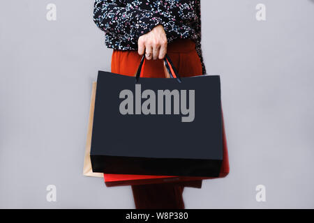 Vue du côté de la récolte de la femme en blouse et pantalon en terre cuite debout avec des sacs de papier dans la main isolé sur fond gris Banque D'Images