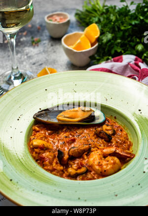 Risotto aux fruits de mer italien, servi avec un verre de vin blanc sec, les citrons et le sel sur fond de béton with copy space Banque D'Images