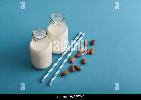 Le lait d'amande dans des bouteilles avec des amandes et pailles sur fond bleu Banque D'Images