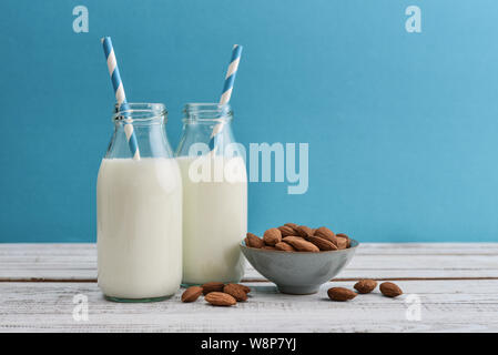 Le lait d'amande dans des bouteilles avec des amandes et pailles sur fond bleu Banque D'Images