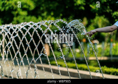 Mettre l'enfant ses doigts dans l'eau d'arrosage d'une fontaine avec des gouttes d'eau détaillée glinstering au soleil Banque D'Images