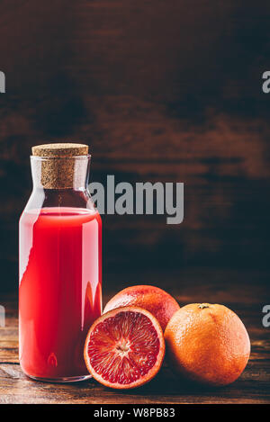 Bouteille de jus d'orange sanguine avec des fruits coupés en deux sur la table en bois Banque D'Images