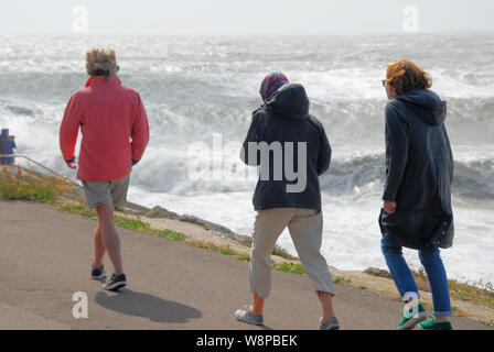 Plage de Chesil. 10 août 2019. Météo britannique. Les jeunes gens pressés, passé à côté de l'énormes vagues battues Chesil Beach, île de Portland. crédit : Alamy Live News Banque D'Images