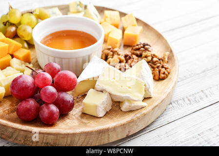 Assiette de fromage - divers types de fromages avec du miel, noix et raisins sur un fond en bois blanc libre Banque D'Images