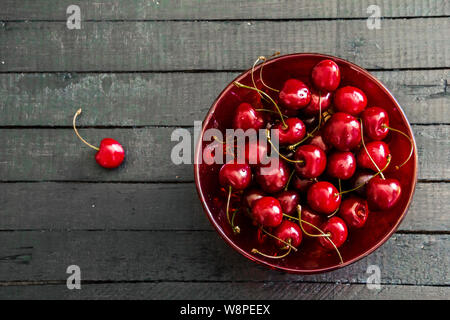 Des produits frais et de cerises mûres dans un bol en verre rouge sur fond noir table de carte en bois . Vue du dessus avec copie espace Banque D'Images