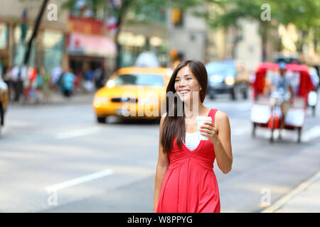 Casual young woman drinking coffee urbain happy smiling à New York, Manhattan. Girl drinking hot drink à partir de gobelet jetable walking in street portant robe rouge avec les taxis jaunes en arrière-plan. Banque D'Images