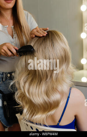 Beau modèle girl blonde avec de longs cheveux bouclés. La création d'Hollywood coiffure vague. Services de coiffure. Des cheveux dénommant des processus. Banque D'Images