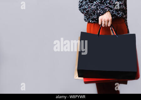 Vue du côté de la récolte de la femme en blouse à motifs et en terre cuite dans des sacs en papier holding pantalon part isolé sur fond gris Banque D'Images