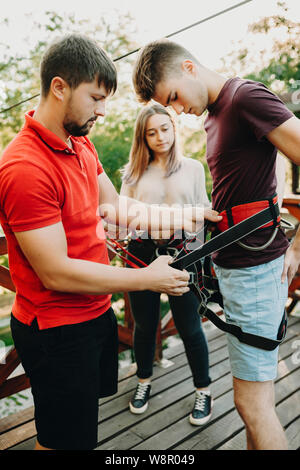 Vue de côté de l'homme aident les jeunes gars avec harnais de sécurité à femme debout près de et la préparation pour la tyrolienne ride Banque D'Images