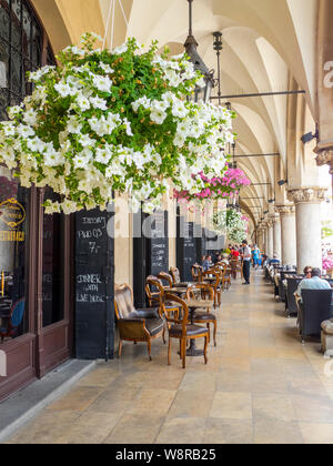 Cracovie, Poland-June 10,2015 : café-restaurant dans les arcades de la halle aux draps de Cracovie avec des chaises en bois et pots de fleurs suspendus Banque D'Images