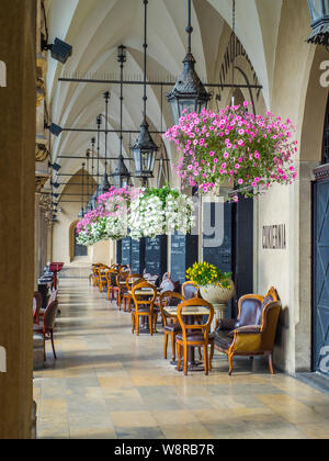 Cracovie, Poland-June 10,2015 : café-restaurant dans les arcades de la halle aux draps de Cracovie avec des chaises en bois et pots de fleurs suspendus Banque D'Images