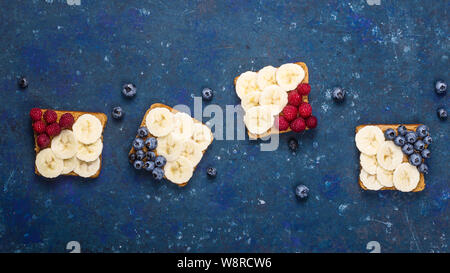 Le petit-déjeuner sandwich sain avec du beurre d'arachide, banane et fruits rouges sur un tableau bleu foncé. Haut de la vue, télévision lay Banque D'Images