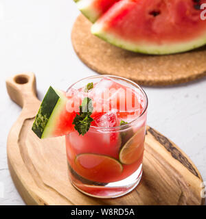 Un verre de jus de melon d'eau froide avec de la glace et garnir de menthe citron vert à côté de quelques morceaux de pastèque en tranches Banque D'Images